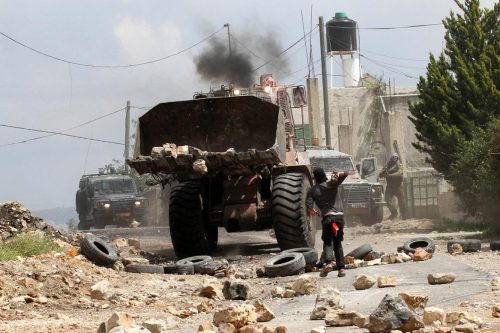 Un manifestante palestino arroja piedras contra un bulldozer israelí en Nablús, Cisjordania.