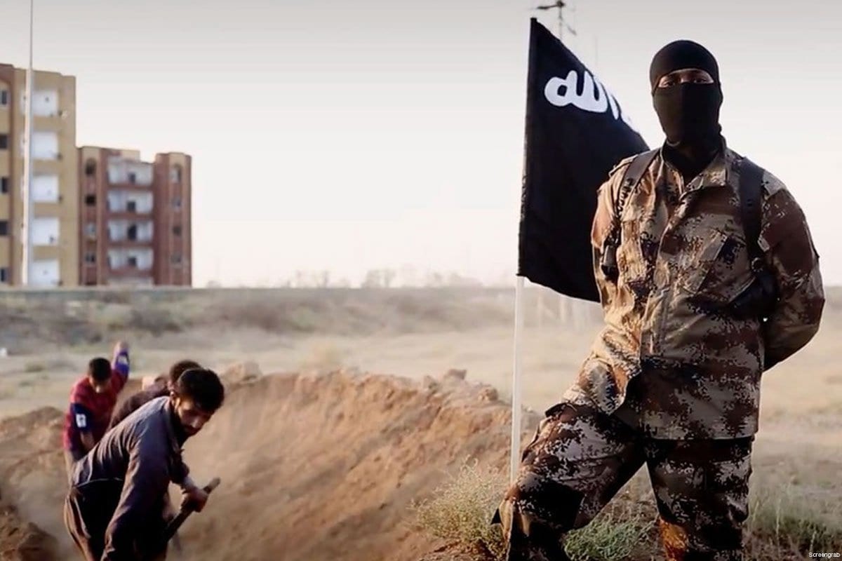 Un combatiente del ISIS frente a un grupo de prisioneros que cavan sus propias tumbas.