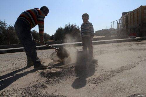 Un hombre palestino recoge la grava que cae de los camiones cargados de cemento después de que ingresó por el cruce de Kerem Shalom en Rafah, para venderla a los clientes, en Gaza